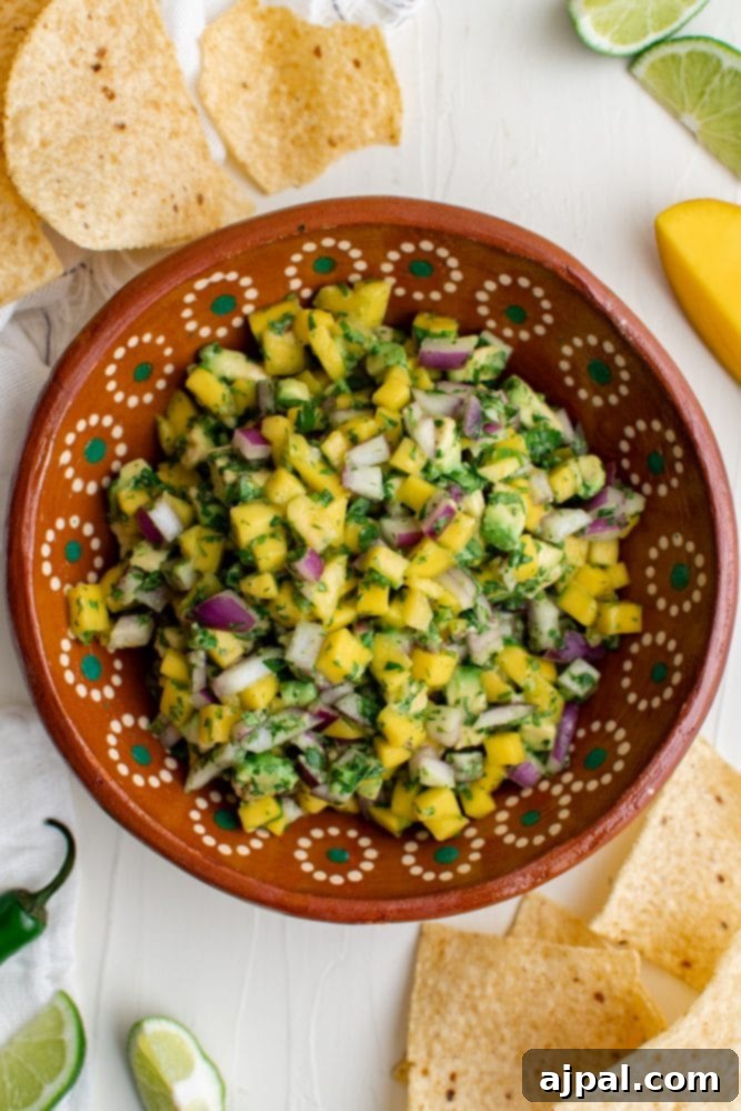 Tropical Mango Avocado Salsa 4 Close-up of mango avocado salsa in a white bowl with tortilla chips around it, garnished with fresh cilantro leaves.