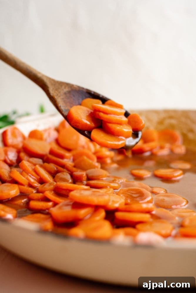 Picture of a wooden spoon stirring brown sugar glazed carrots in a pan.