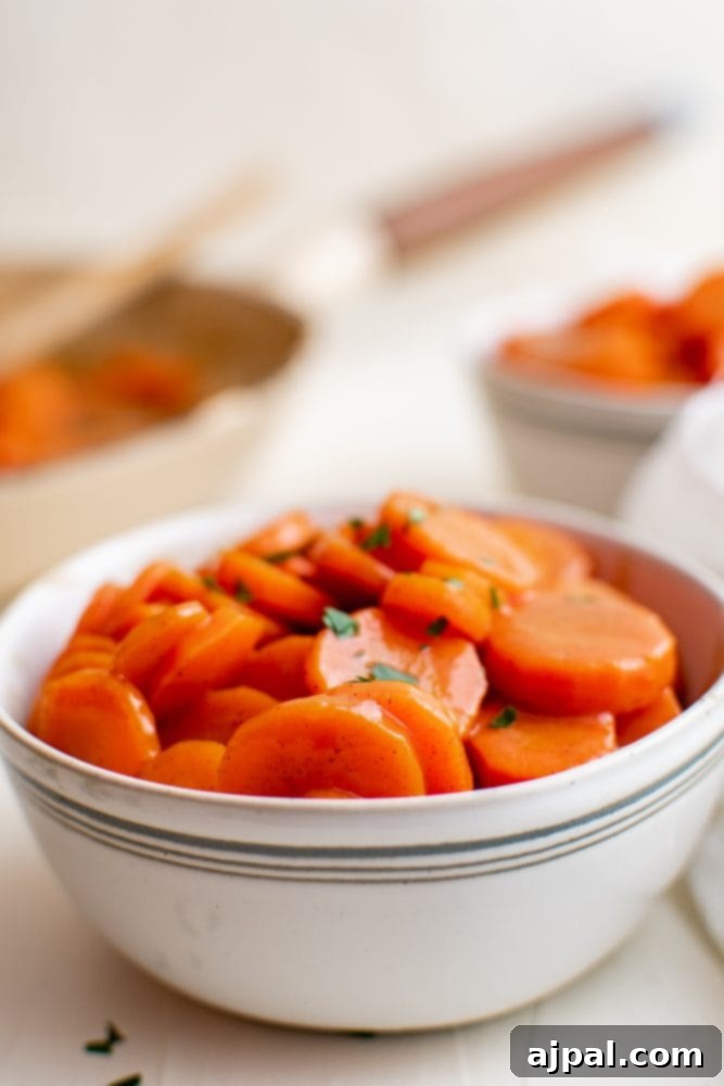 Picture of a pan of sugar glazed carrots resting on a wooden table, next to a cooking pan.