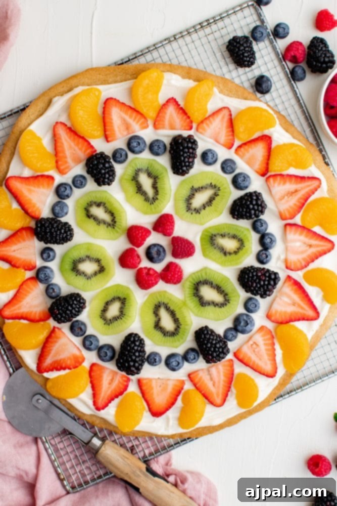 Effortless Rainbow Fruit Pizza 2 A beautifully arranged fruit pizza with vibrant berries and sliced kiwis, resting on a cooling rack. The dessert features a golden cookie base and a smooth, creamy frosting layer.