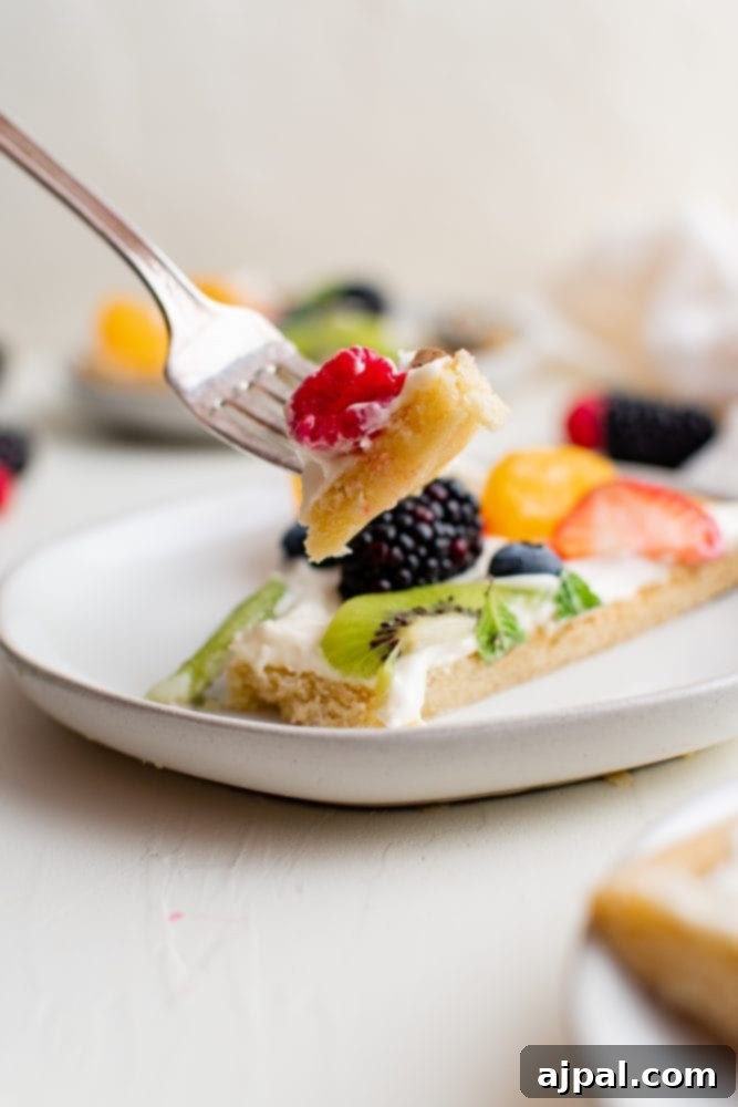 Effortless Fruit Pizza Perfection 13 A delectable fruit pizza, freshly sliced and ready to enjoy, with one perfect piece on a fork, showcasing its crisp cookie base, creamy topping, and colorful fruit.