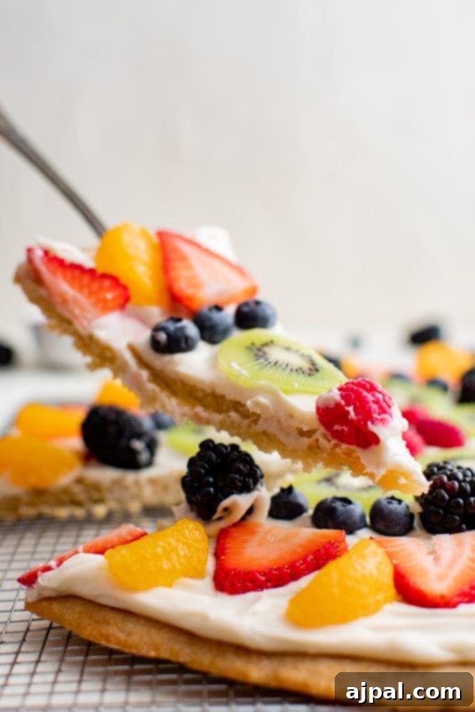 Effortless Fruit Pizza Perfection 3 A single slice of homemade fruit pizza on a white plate, showcasing the fluffy cream cheese topping and vibrant mixed berries and kiwi on a golden sugar cookie crust.