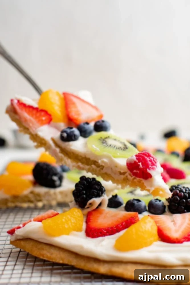Effortless Rainbow Fruit Pizza 3 A close-up of a single slice of fruit pizza, revealing the crisp cookie base, thick creamy frosting, and an assortment of colorful berries.