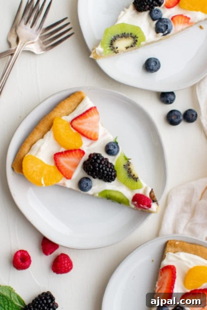 Effortless Rainbow Fruit Pizza 19 Two generous slices of fruit pizza, highlighting the vibrant fruit toppings and creamy layer, presented on a white surface.