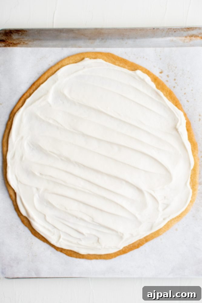 Effortless Fruit Pizza Perfection 15 A large, perfectly round sugar cookie crust generously covered with a smooth, white cream cheese topping, ready for fruit.