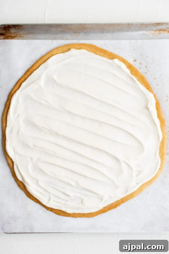 Effortless Rainbow Fruit Pizza 14 A freshly baked sugar cookie crust with an even layer of creamy white frosting spread across it, ready for fruit.