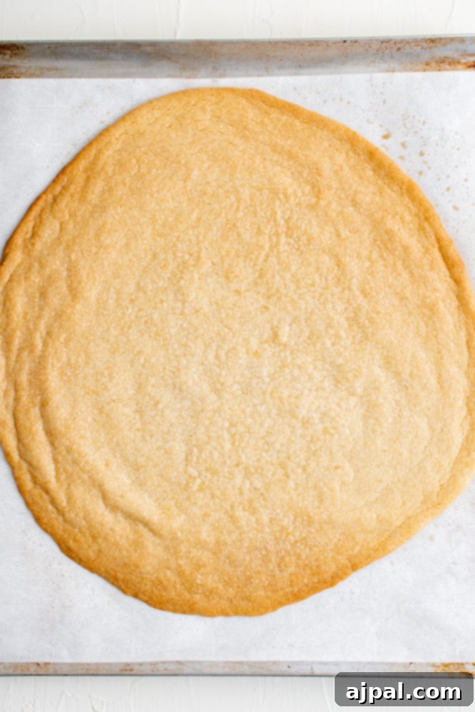 Effortless Fruit Pizza Perfection 7 A large, perfectly baked sugar cookie crust on parchment paper, golden brown at the edges and ready for topping.