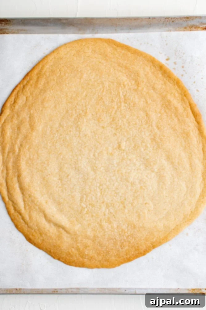 Effortless Rainbow Fruit Pizza 7 A large, golden-baked sugar cookie crust cooling on baking paper, awaiting its creamy topping and fresh fruit.
