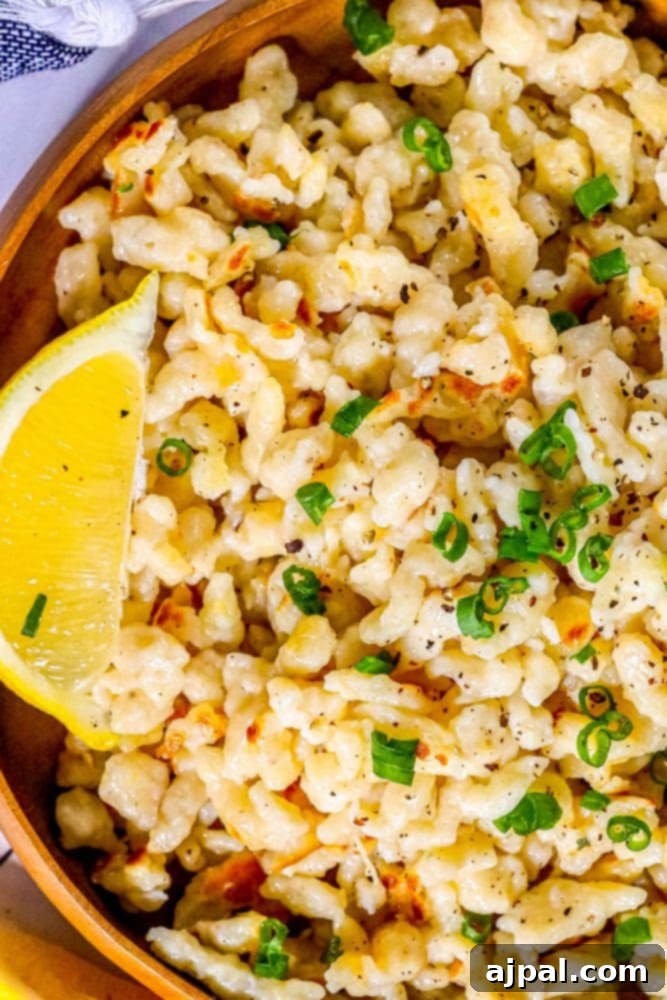 A rustic wooden bowl brimming with golden-brown Spaetzle, garnished with fresh green onions and a lemon wedge, embodying authentic German comfort food.