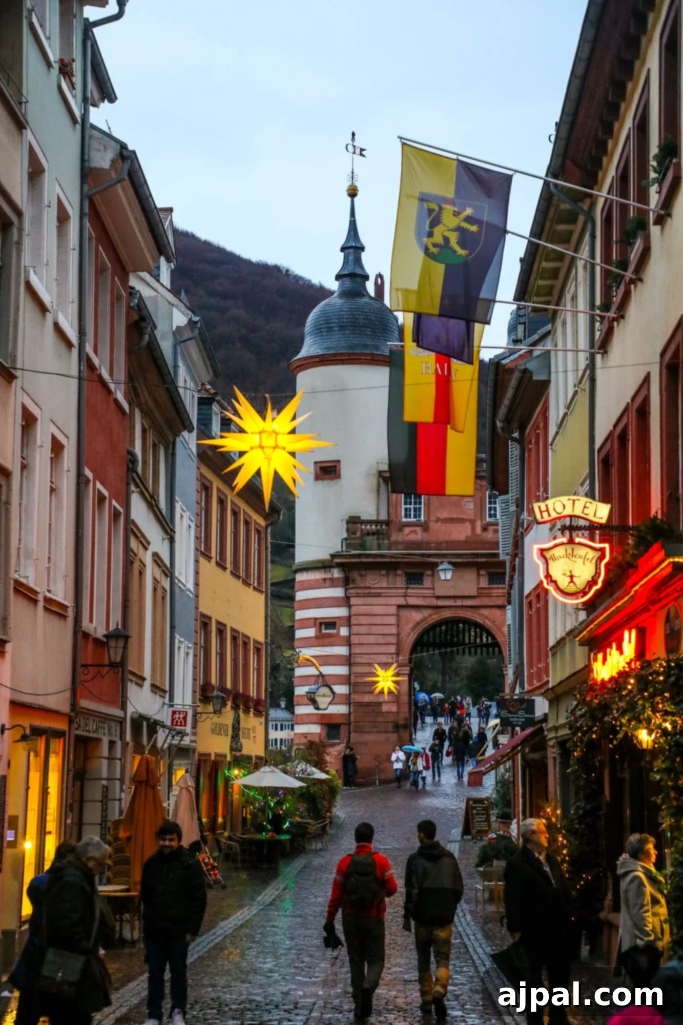 A festive Christmas market scene in Heidelberg, Germany, with people strolling along a cobblestone street.
