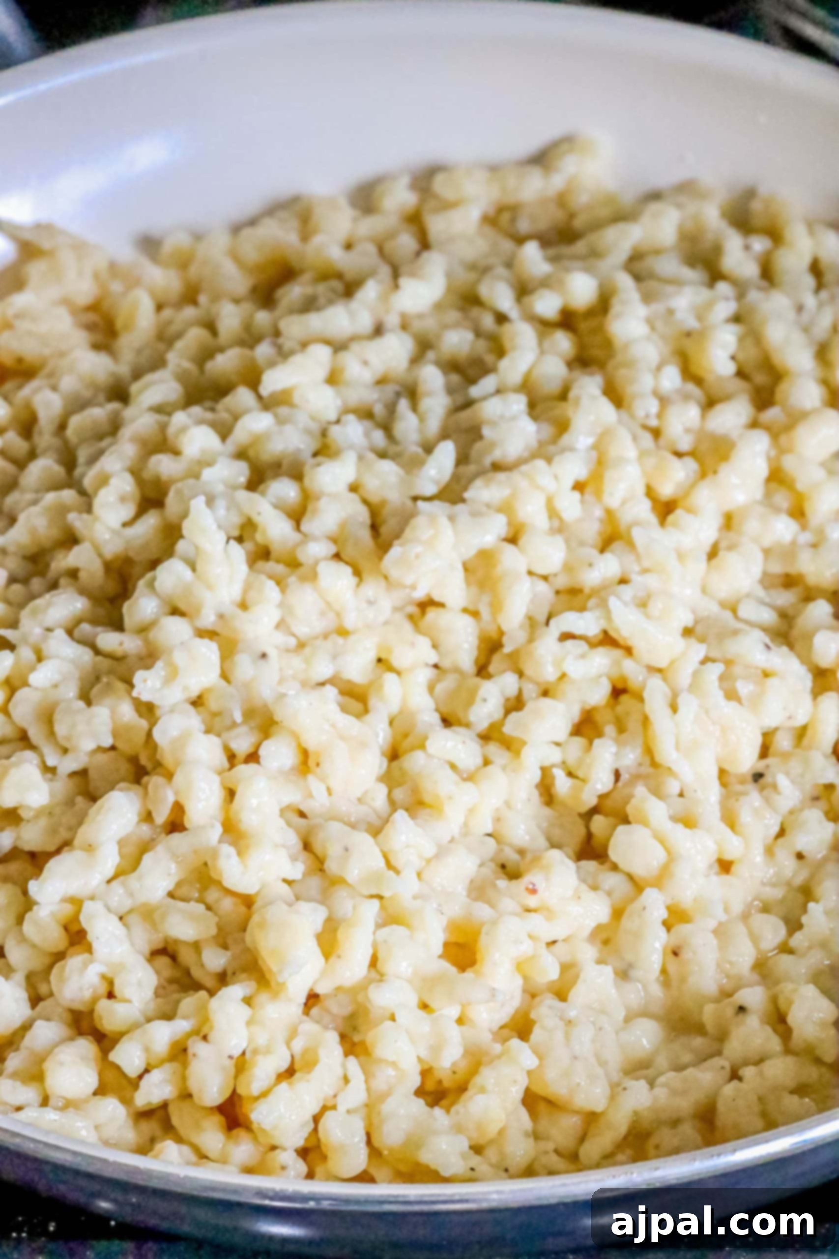 Golden-brown Spaetzle frying in melted butter in a nonstick pan, creating a crispy texture.