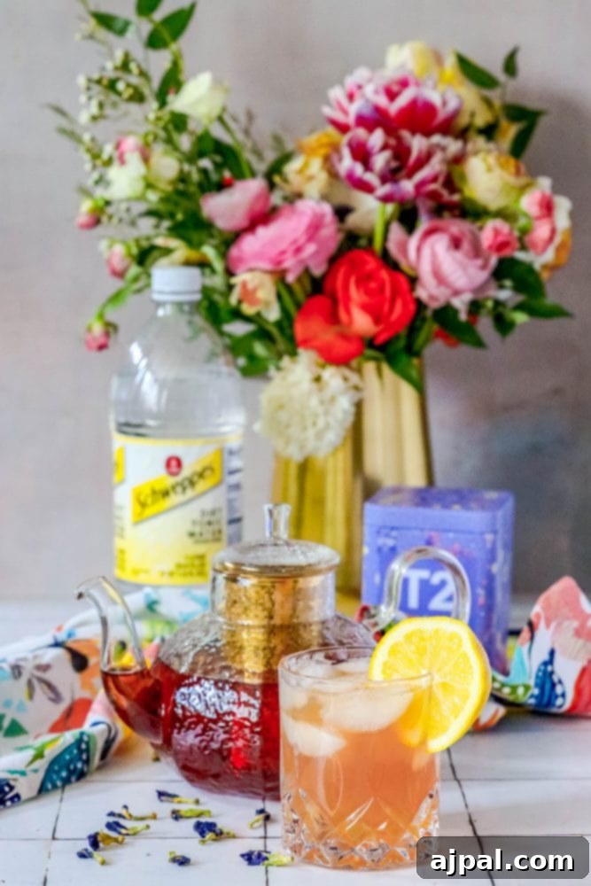Bubbly Earl Grey Tea Tonic 3 A glass of sparkling tea and tonic mocktail adorned with fresh flowers on a elegant table setting.