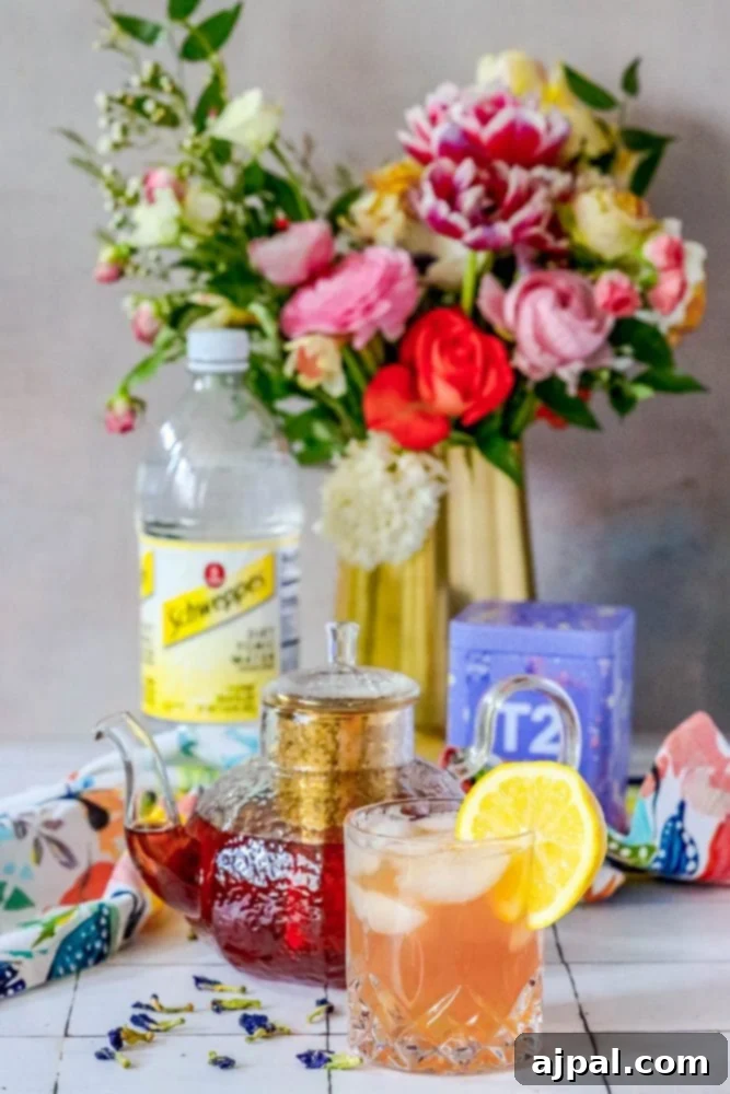 Sparkling Earl Grey Tonic Recipe 3 A elegant tea set featuring a teapot and a sparkling tea and tonic mocktail, adorned with delicate flowers on a table, creating an inviting and refreshing scene.