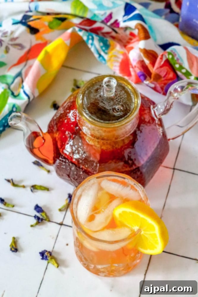 Sparkling Earl Grey Tonic Recipe 4 A vibrant cocktail garnished with a lemon wedge, positioned in front of a teapot, creating an inviting visual of the Earl Grey Sparkling Tea and Tonic mocktail.
