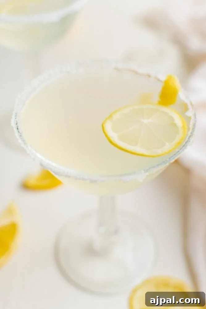 A dazzling Lemon Drop Martini, garnished with a fresh lemon slice and a sugar-rimmed glass, glowing with its inviting light yellow hue.