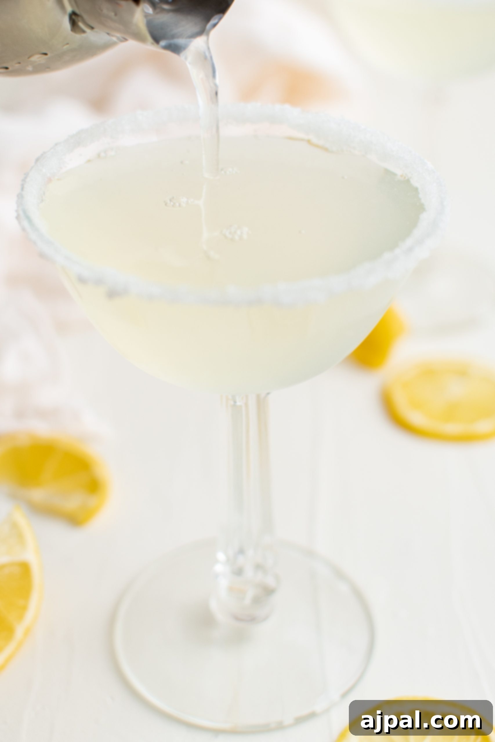 Zesty Lemon Drop Martini Recipe 7 A lemon drop martini being poured into a glass with lemon slices.