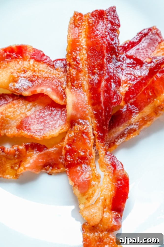 Beautifully cooked bacon on a pristine white plate, showcasing the perfect crispiness achieved through oven baking.