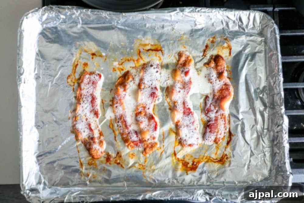 Bacon baked in oven wrapped in foil on a baking sheet.