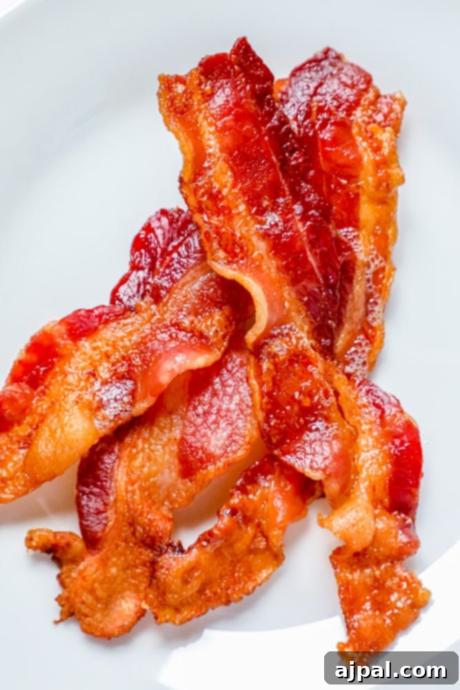 Golden-brown, perfectly cooked bacon resting on a white plate after being baked in the oven.