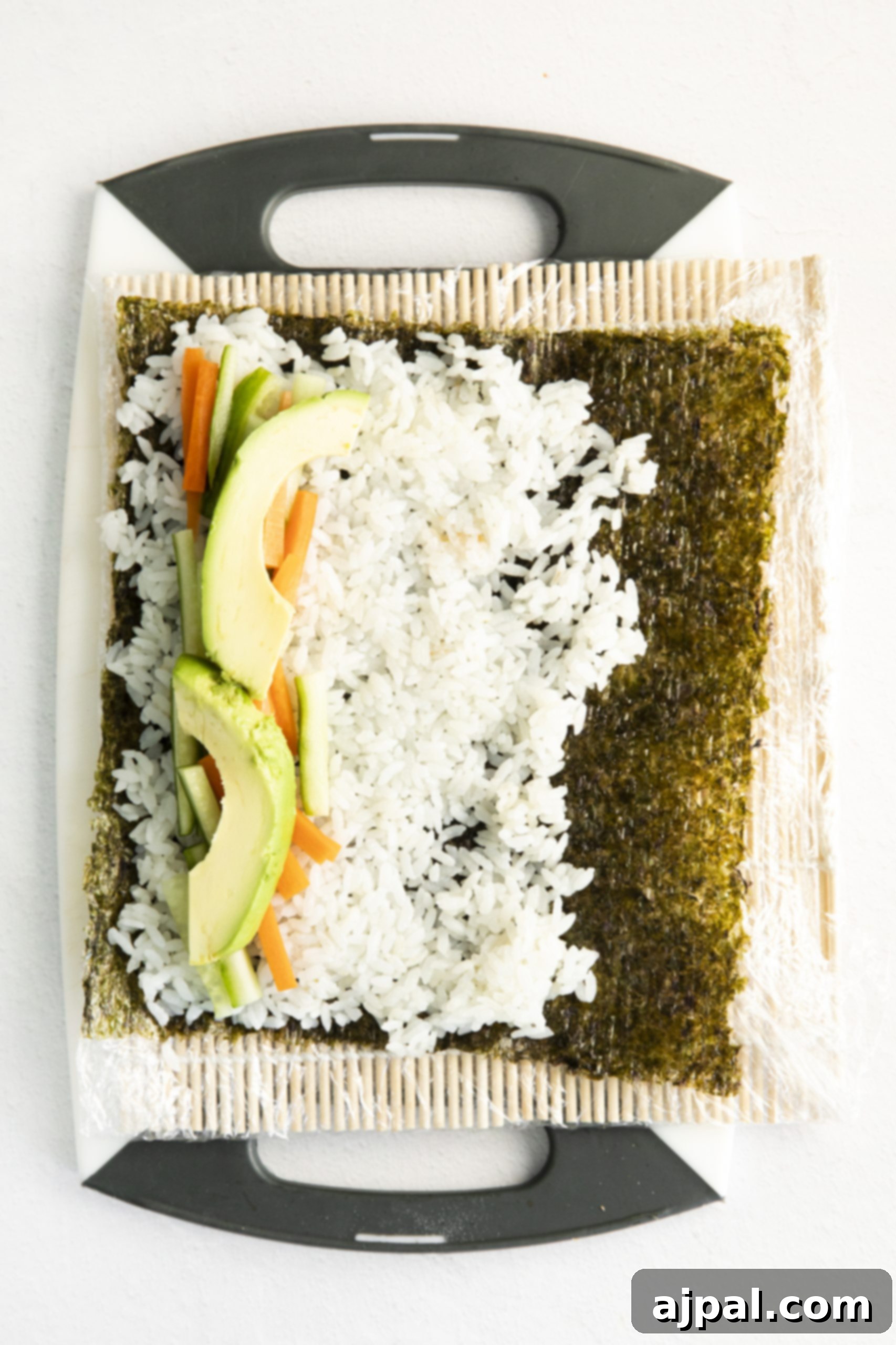 Effortless Vegan Sushi Rolls 11 A vegan vegetable sushi recipe featuring a sheet of rice and vegetables on a cutting board.