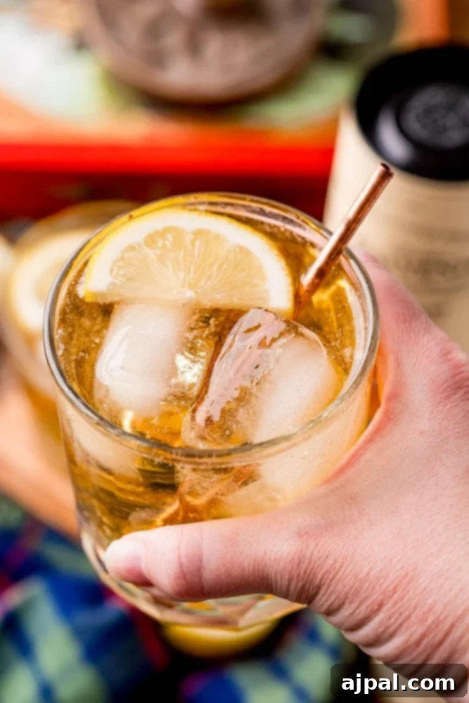 A hand holding a glass of whisky, also known as scotch, with a slice of lemon, showcasing the ready-to-drink cocktail.