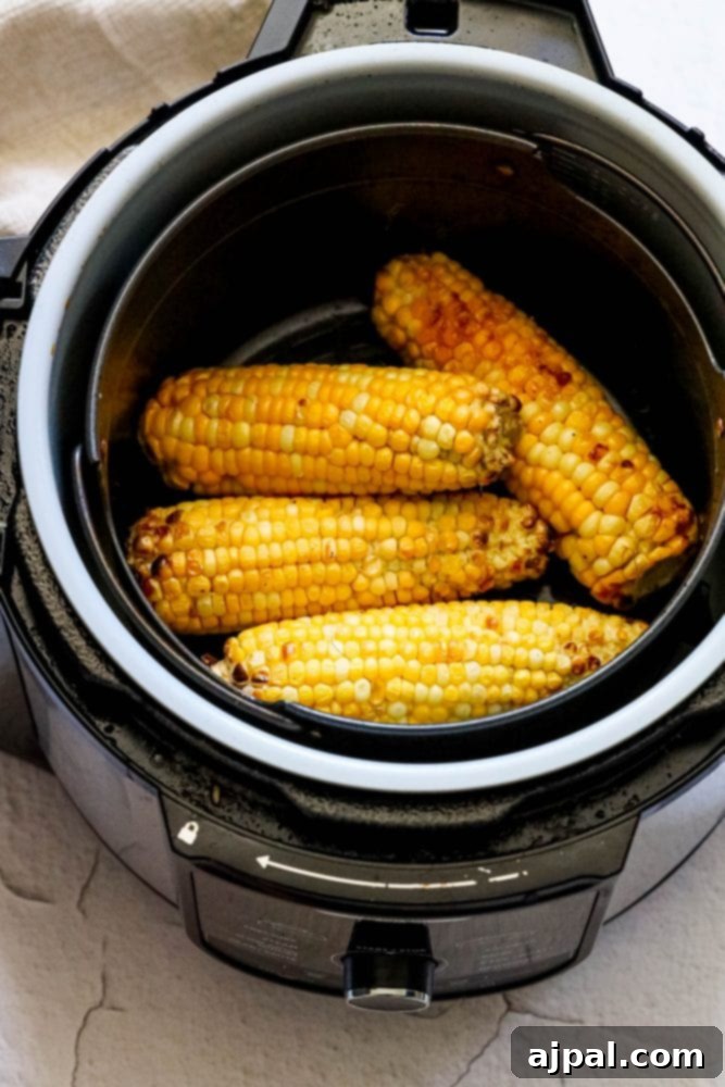 Freshly shucked corn ears glistening inside an air fryer basket, ready for cooking.