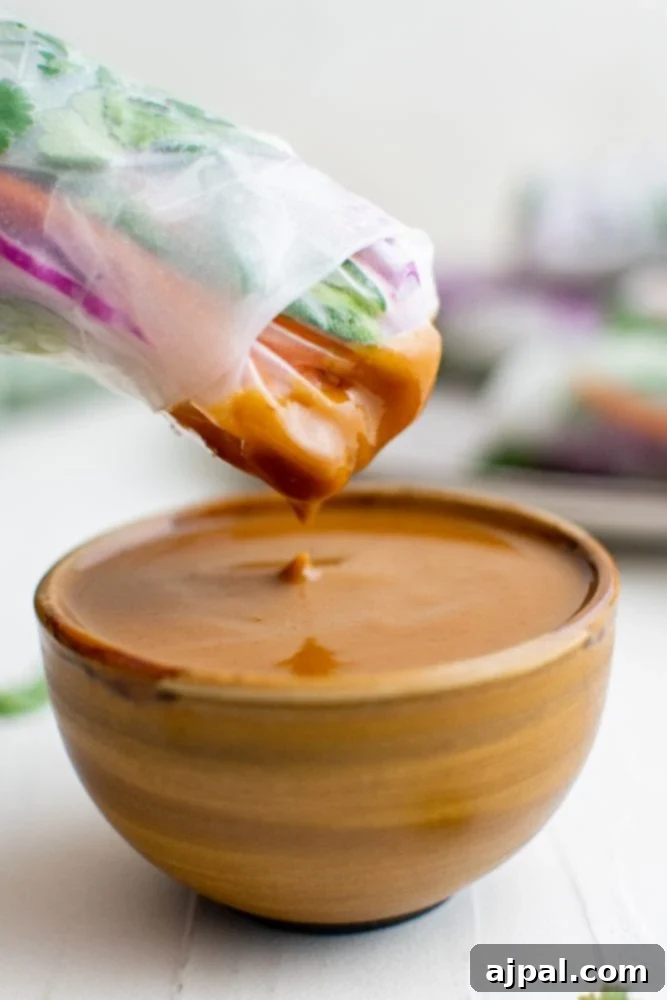 A fresh spring roll being dipped into a rich, creamy homemade peanut sauce, showcasing its perfect consistency.