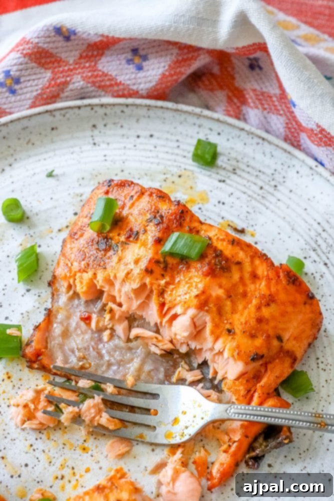 Easy Air Fryer Jerk Salmon 7 A plate of air fryer jerk salmon with a fork, showing the crispy skin and tender flesh.