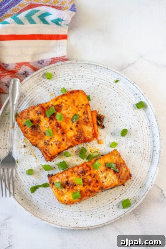 Easy Air Fryer Jerk Salmon 8 A beautifully grilled salmon fillet, ready to eat, on a white plate with a fork.