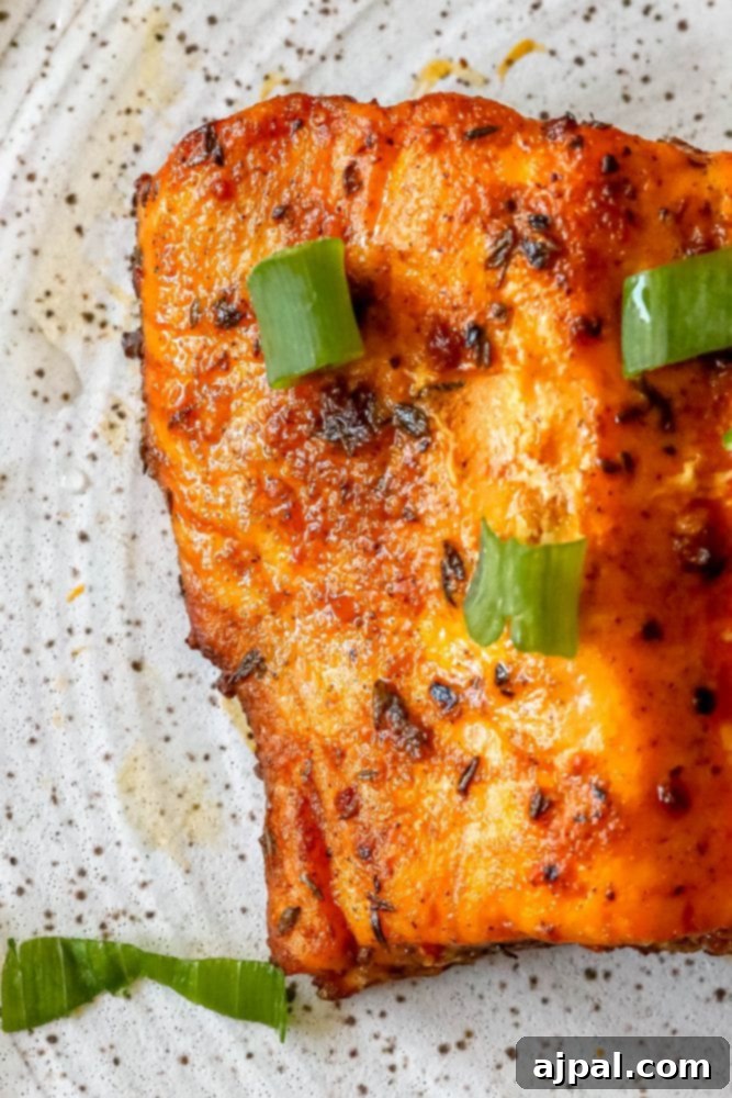 Easy Air Fryer Jerk Salmon 5 A vibrant air-fried jerk salmon fillet, seasoned with spices, on a white plate with green onions.