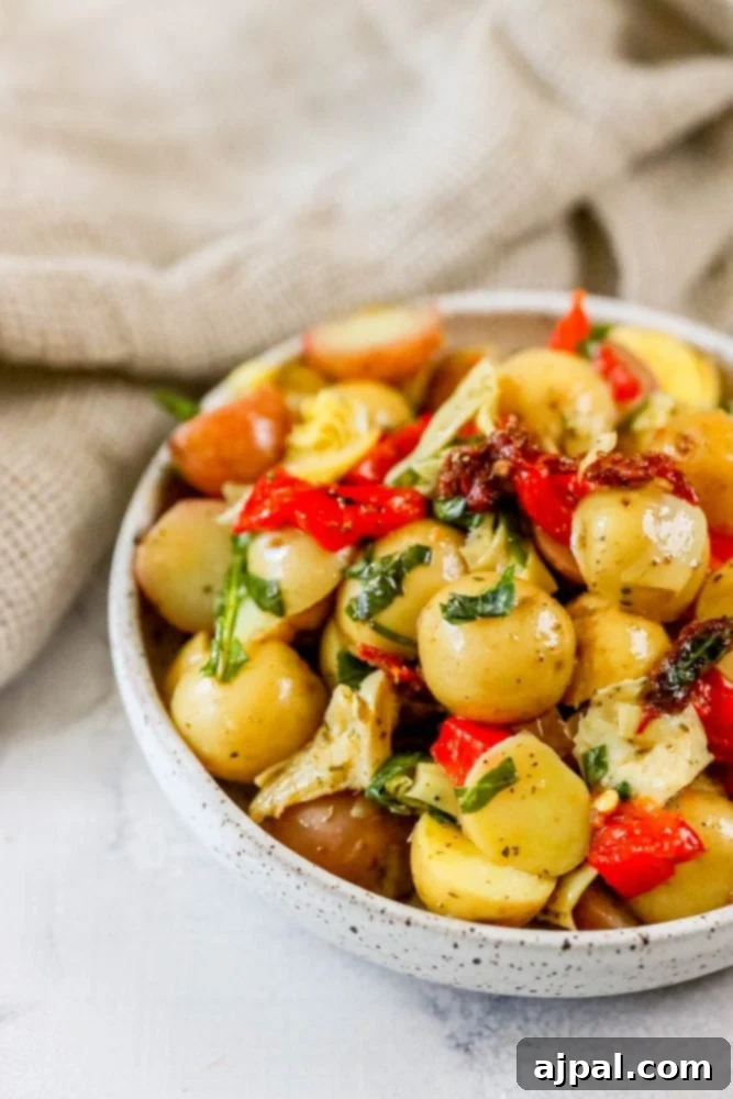 Zesty Italian Potato Salad 2 A beautifully arranged bowl of Italian Potato Salad featuring golden potatoes, fresh green basil, marinated artichoke hearts, vibrant sun-dried tomatoes, and strips of roasted red peppers, all lightly coated in an olive oil dressing.