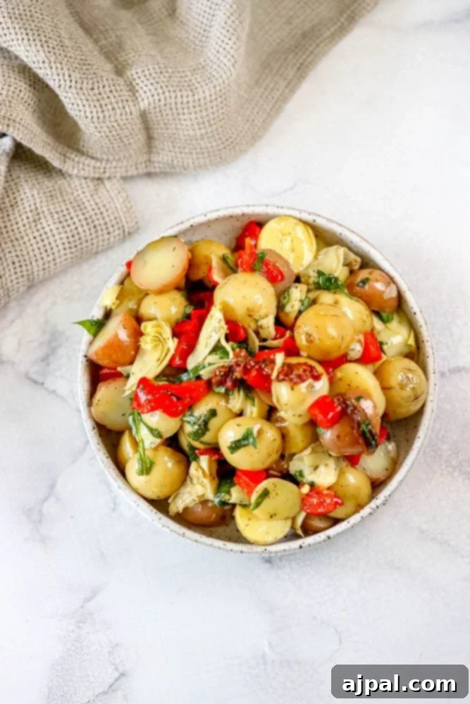 Zesty Italian Potato Salad 3 A large bowl of delicious Italian Potato Salad, generously drizzled with olive oil, showcasing sliced potatoes, roasted red peppers, and fresh herbs on a rustic marble table, ready to be served.