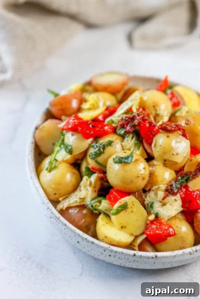 Zesty Italian Potato Salad 5 A vibrant bowl of Italian Potato Salad, generously garnished with fresh basil, showcasing tender potatoes, roasted red peppers, sun-dried tomatoes, and artichoke hearts, ready to be enjoyed.