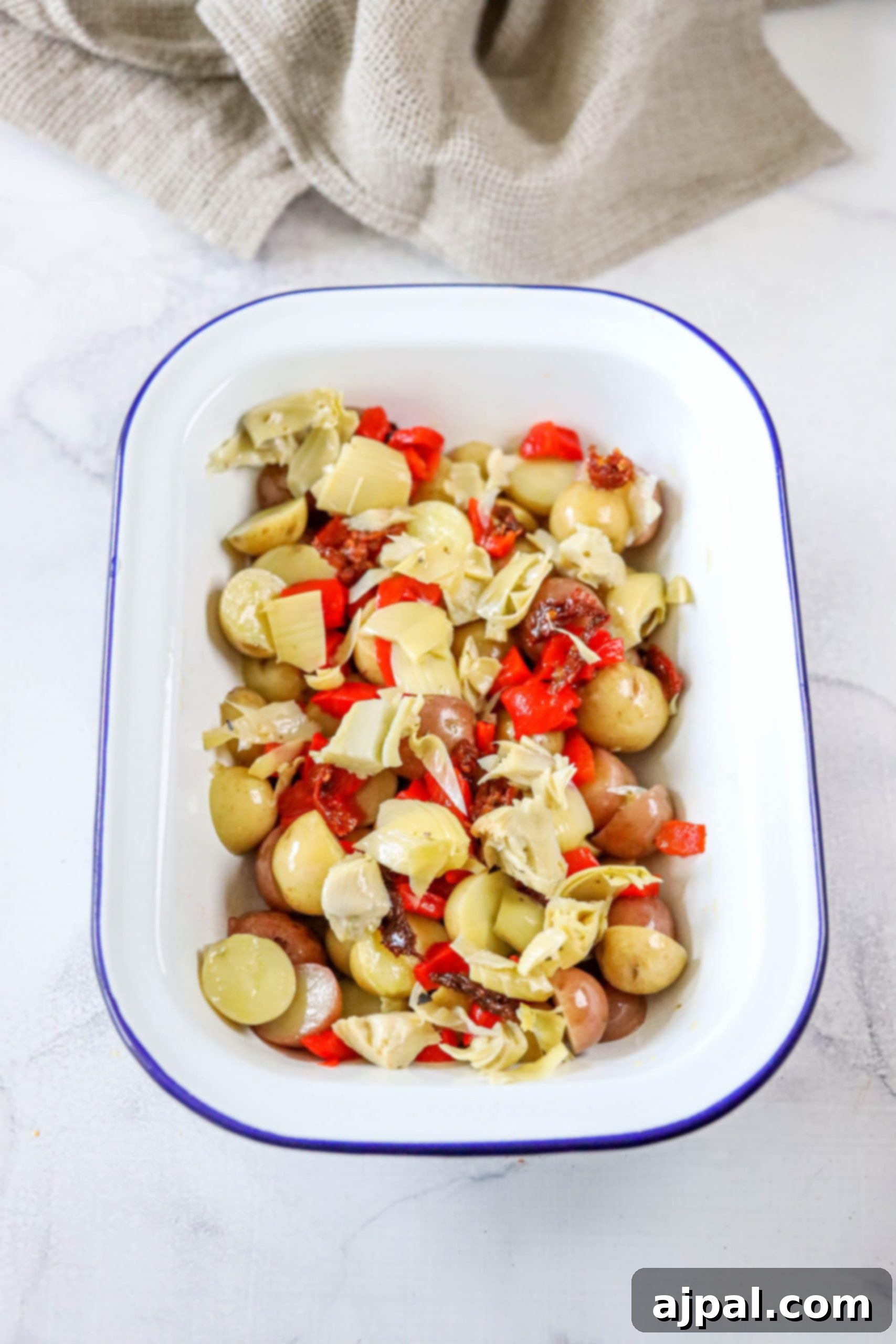 Zesty Italian Potato Salad 8 An appetizing platter of Italian Potato Salad, featuring a delightful combination of potatoes, roasted red pepper strips, artichoke hearts, and sun-dried tomatoes.