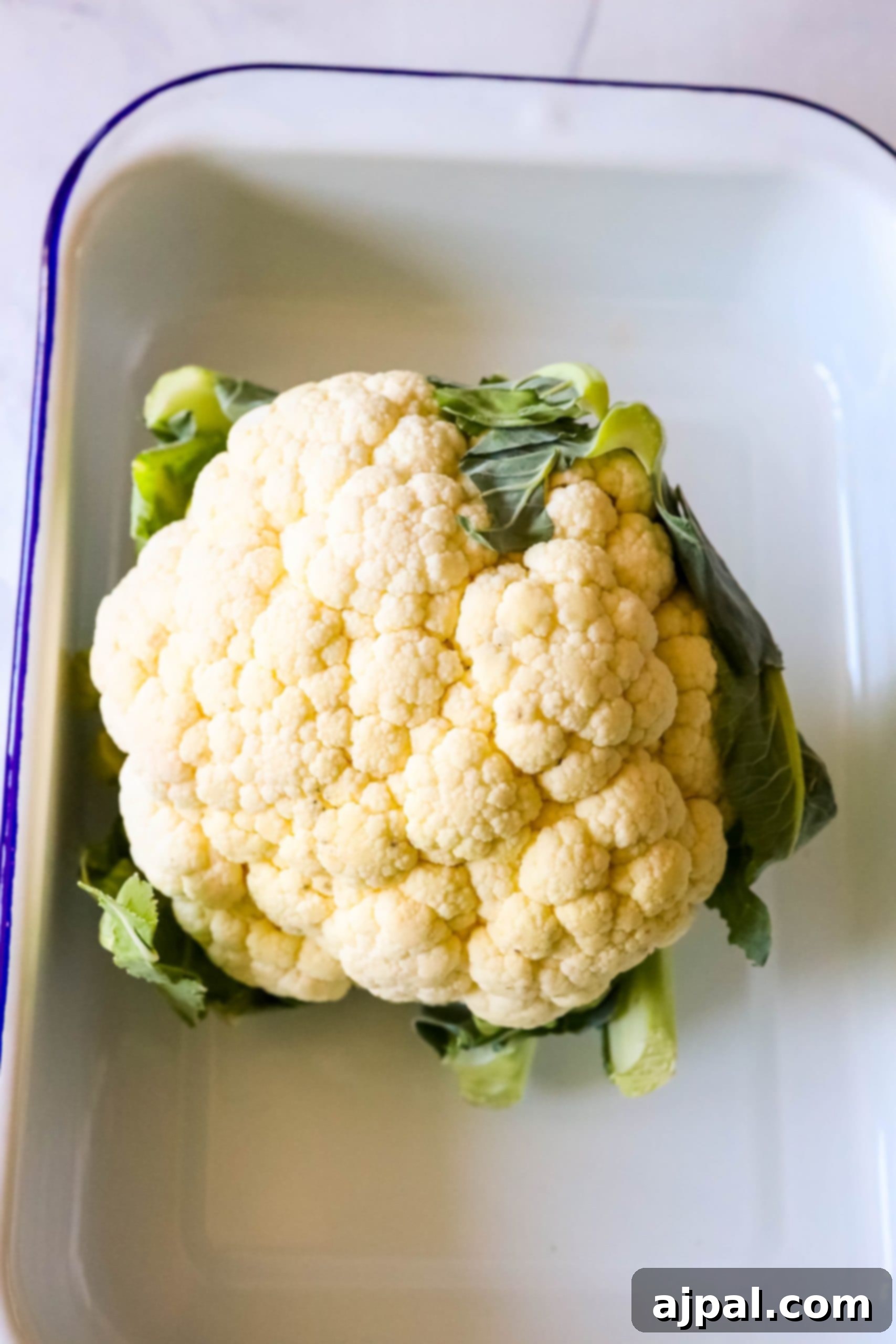A whole roasted cauliflower in a blue and white dish.