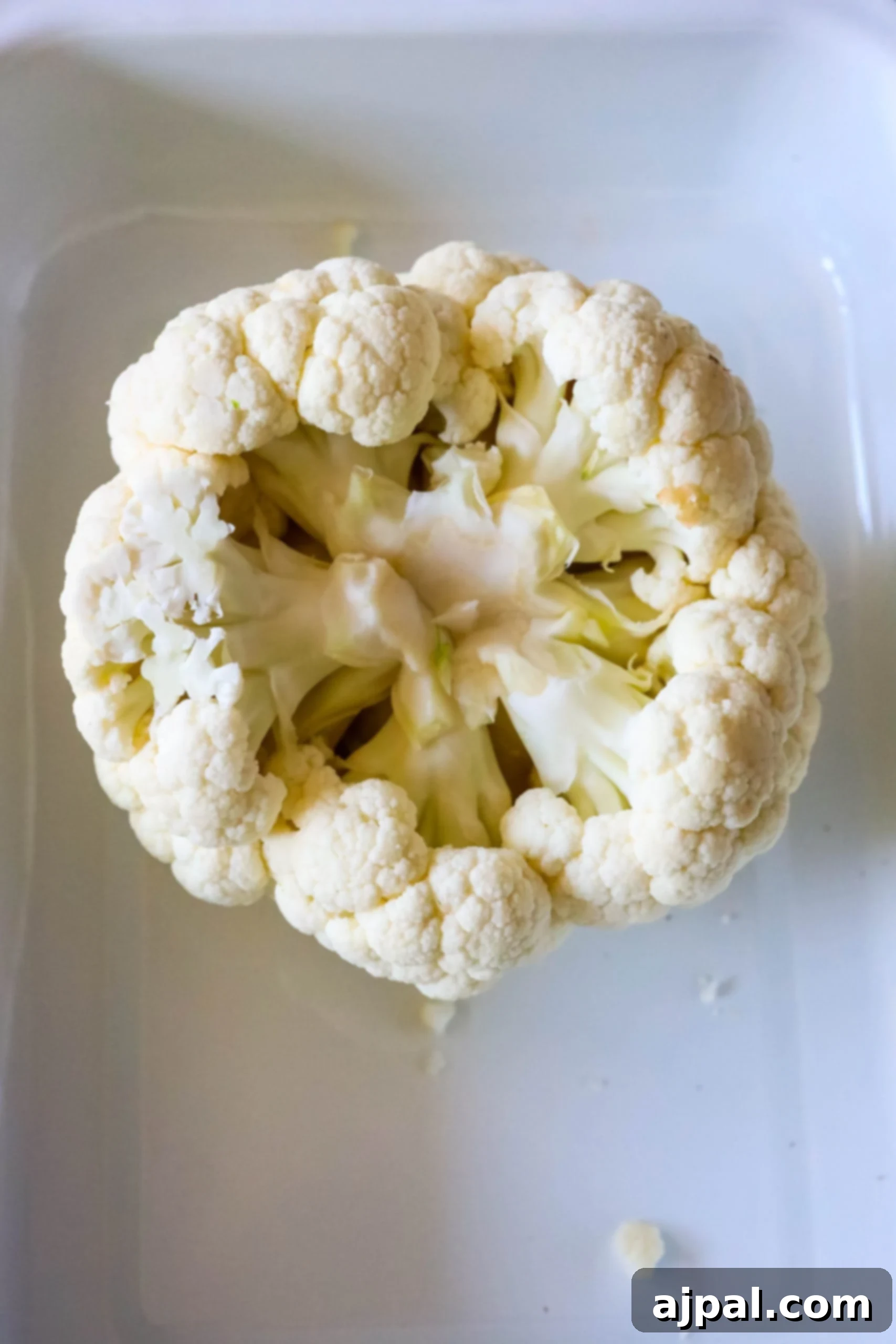 Whole roasted cauliflower in a white dish on a table.