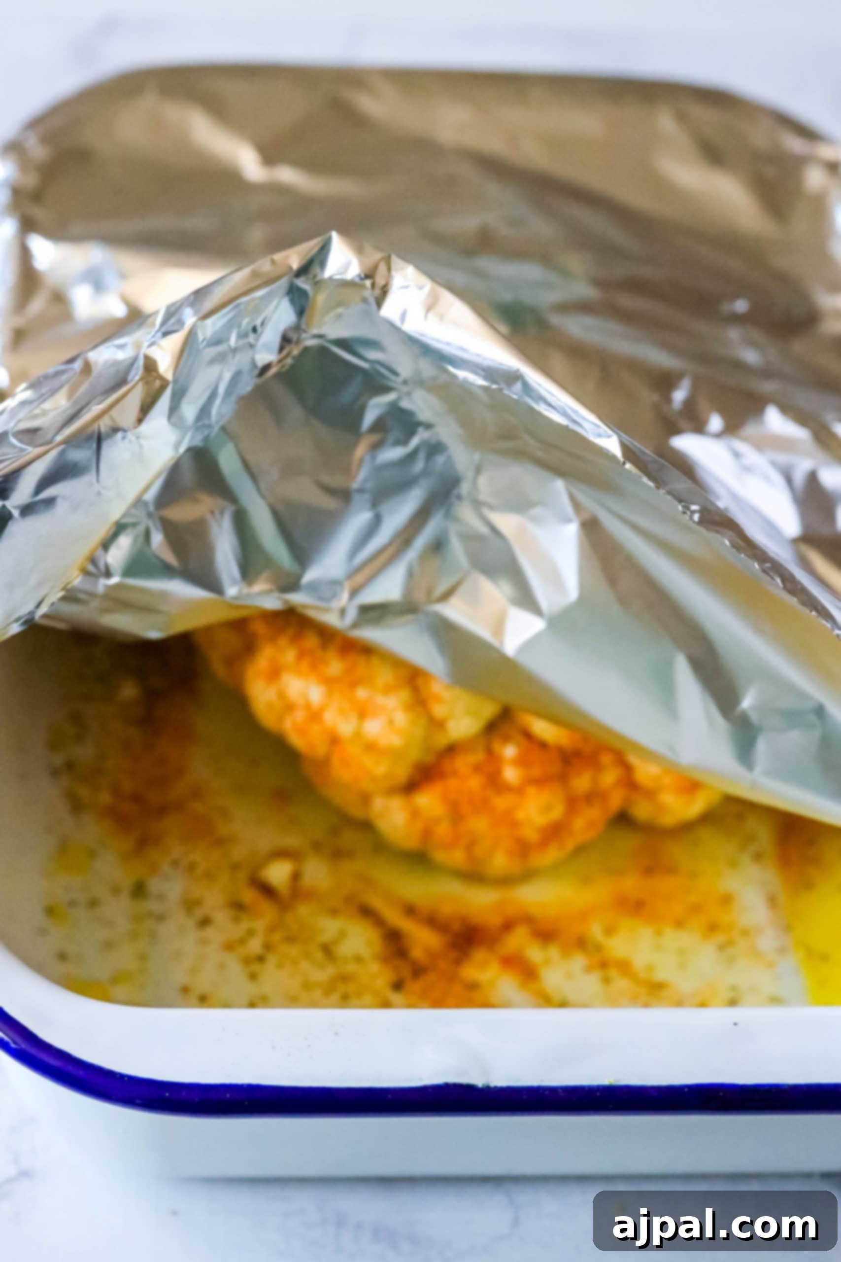 Foil wrapped chicken in a baking dish, keto roasted cauliflower.