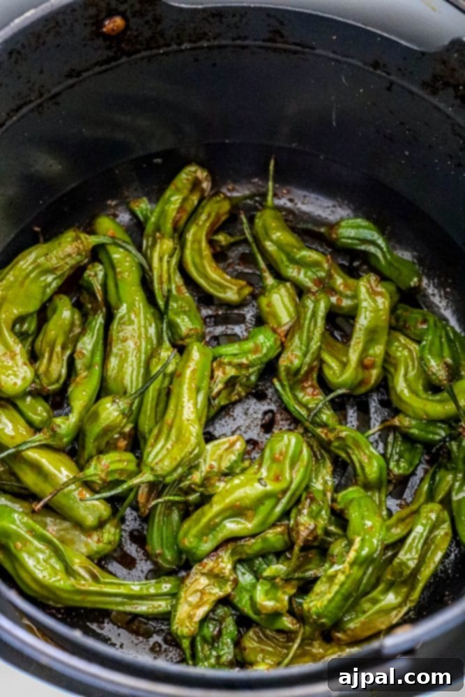 Shishito peppers being cooked in an air fryer basket, showing early signs of charring and tenderness.