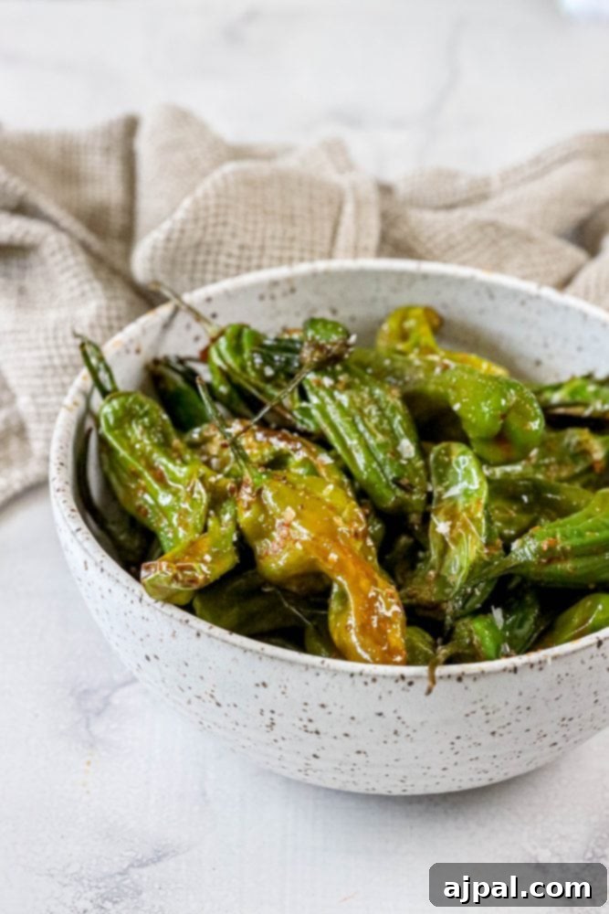 Green shishito peppers perfectly arranged and cooked in an air fryer basket, showing their charred and tender state.