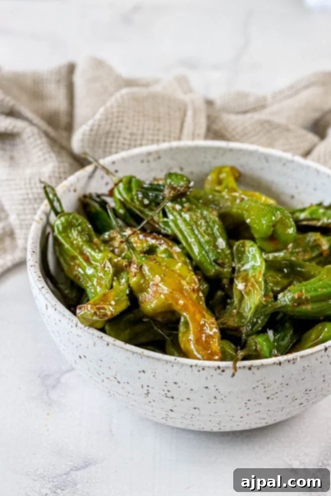 Crispy Air Fryer Shishito Peppers 5 Green shishito peppers being tossed in an air fryer basket, showing their uniform charring.