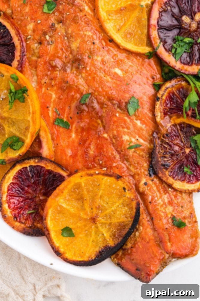 Delicious baked salmon with a vibrant orange glaze, garnished with browned orange slices and fresh chopped parsley on a white platter, ready to be served on a table.