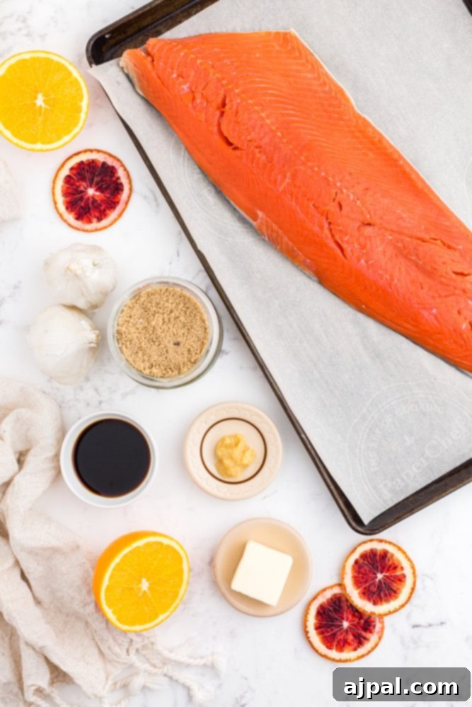 Fresh ingredients laid out on a table: a salmon fillet, whole ginger, sliced oranges, minced garlic, soy sauce, butter, and brown sugar, ready for making the glaze.
