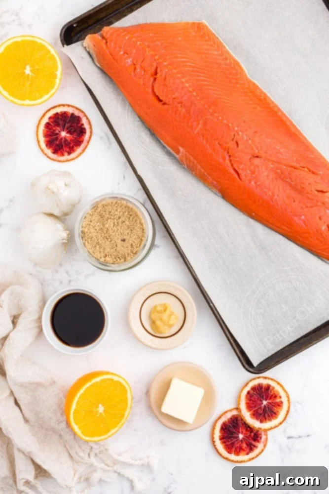 A collection of fresh ingredients for orange-glazed salmon: raw salmon fillet, sliced ginger, fresh orange slices, garlic cloves, soy sauce, butter, and brown sugar, arranged on a rustic wooden table.