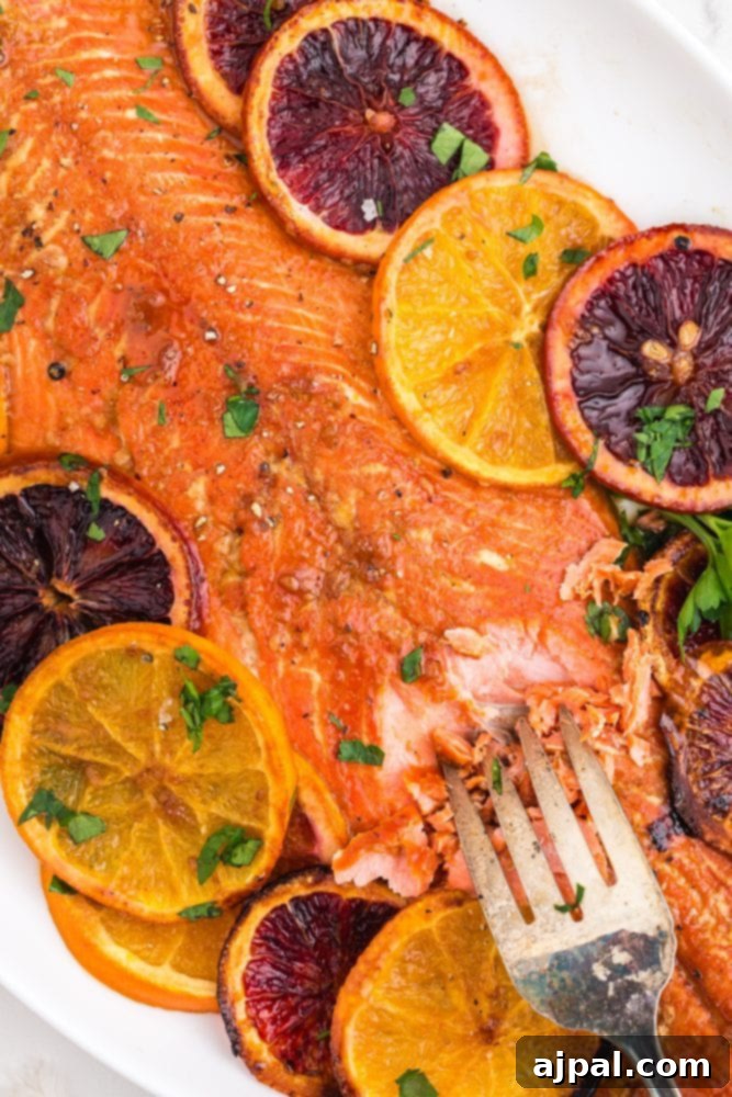 A serving of orange glazed salmon on a white plate, accompanied by fresh orange slices and a fork, highlighting the tender, flaky texture of the fish.
