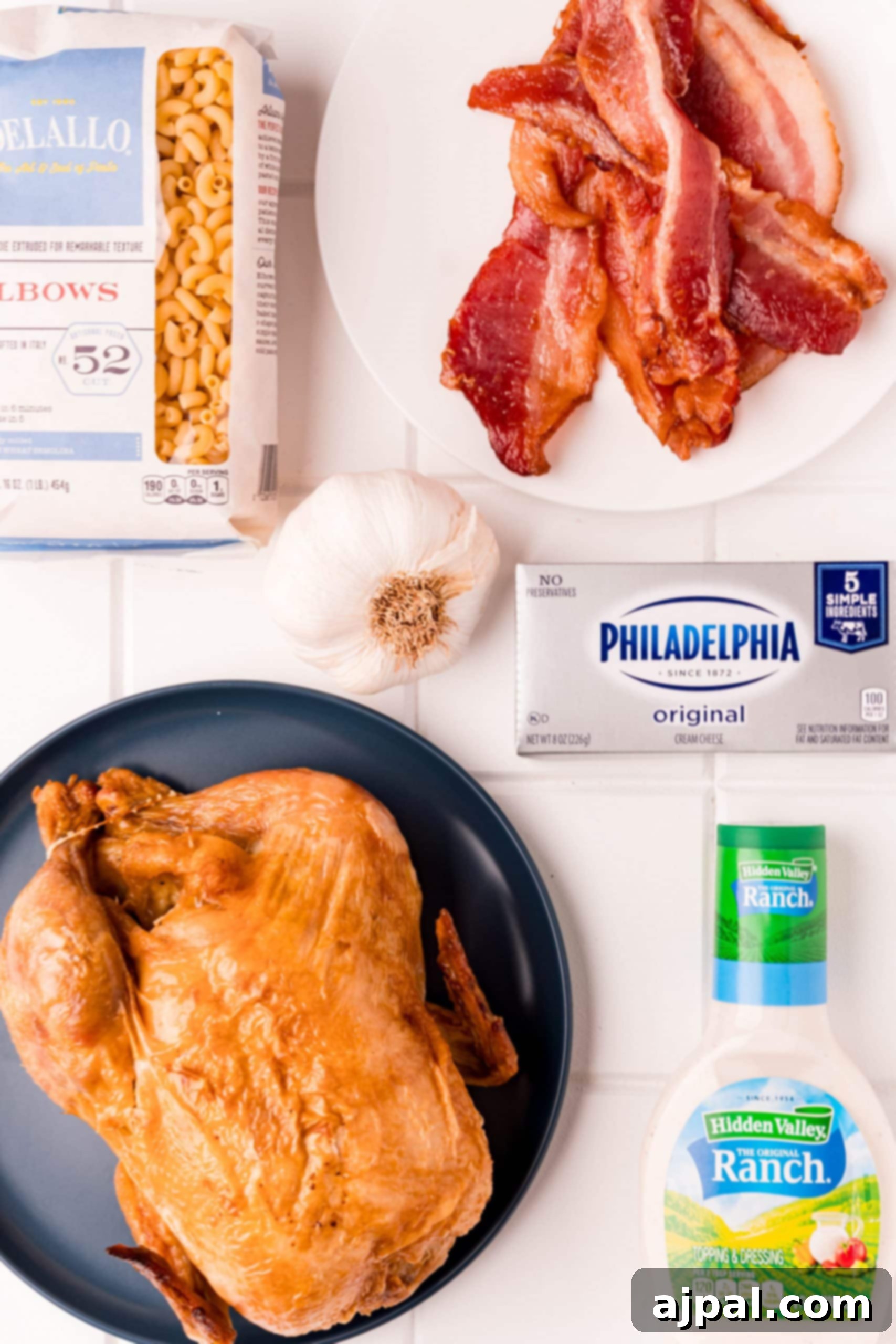 Loaded Bacon Ranch Chicken Mac and Cheese 5 A vibrant selection of fresh ingredients including a whole rotisserie chicken, crispy bacon, a jar of ranch dressing, and garlic, laid out on a wooden table, ready for preparation.