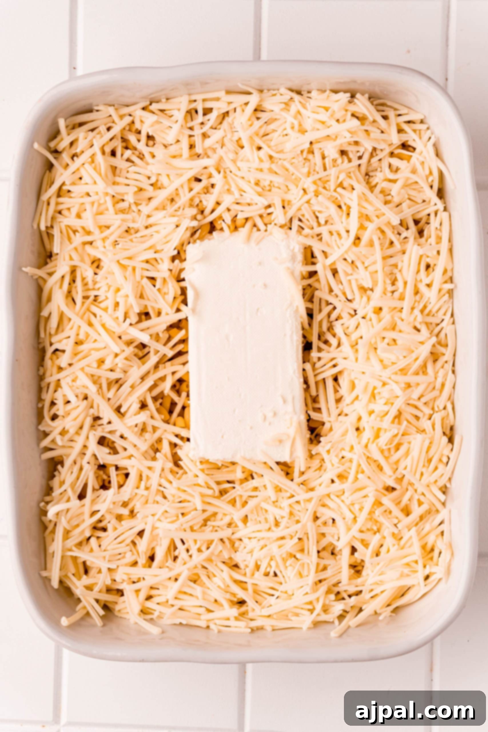 Loaded Bacon Ranch Chicken Mac and Cheese 6 A baking dish containing cooked pasta, shredded cheddar, and milk, with a block of cream cheese placed centrally, ready for initial stirring to create the base of the creamy sauce.