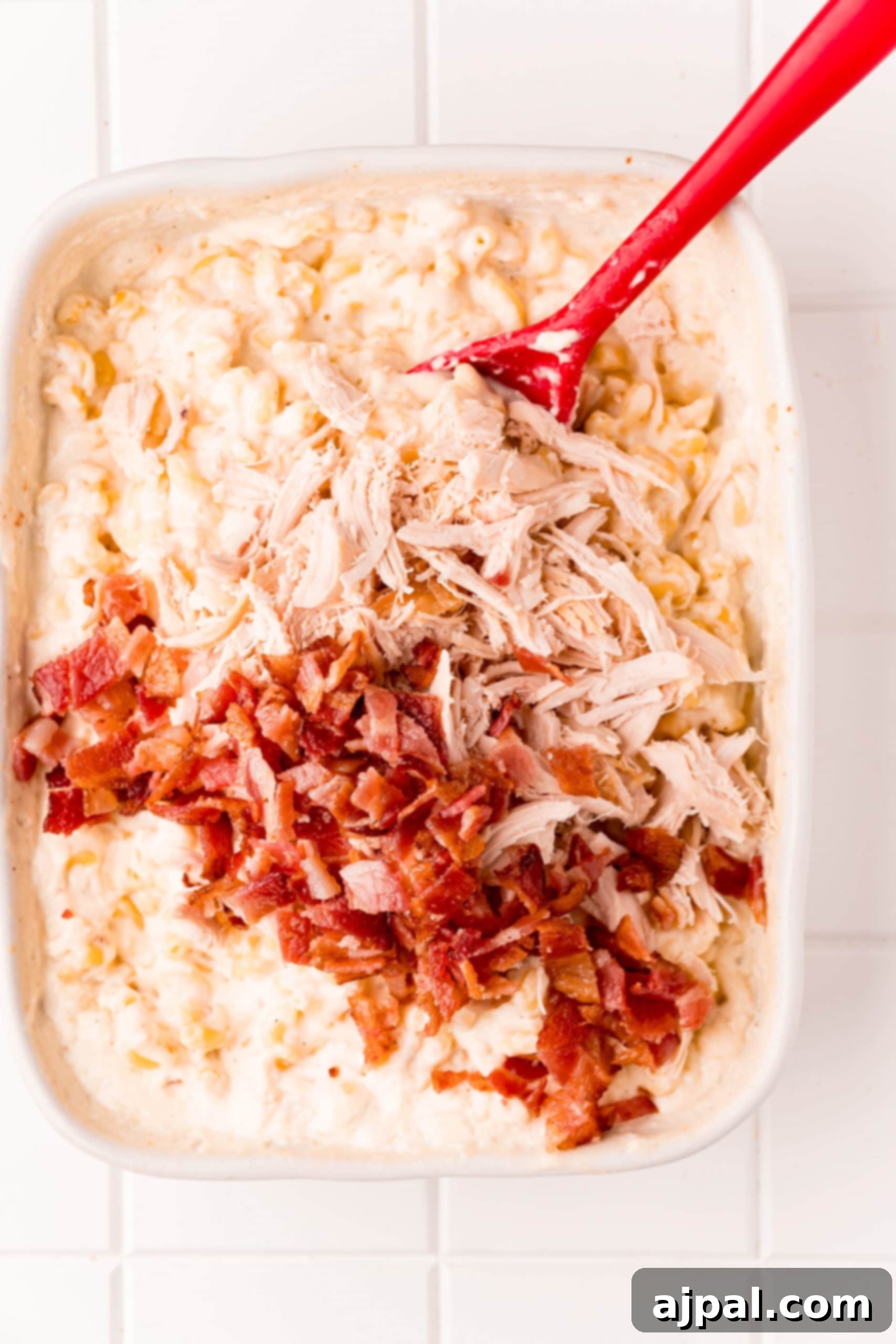 Loaded Bacon Ranch Chicken Mac and Cheese 8 Cooked chicken and crispy bacon pieces being gently stirred into a pan of hot, creamy macaroni and cheese, ensuring even distribution.