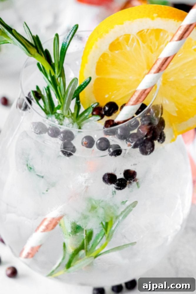 A glass of gin with rosemary and blackberries, garnished with cardamom.