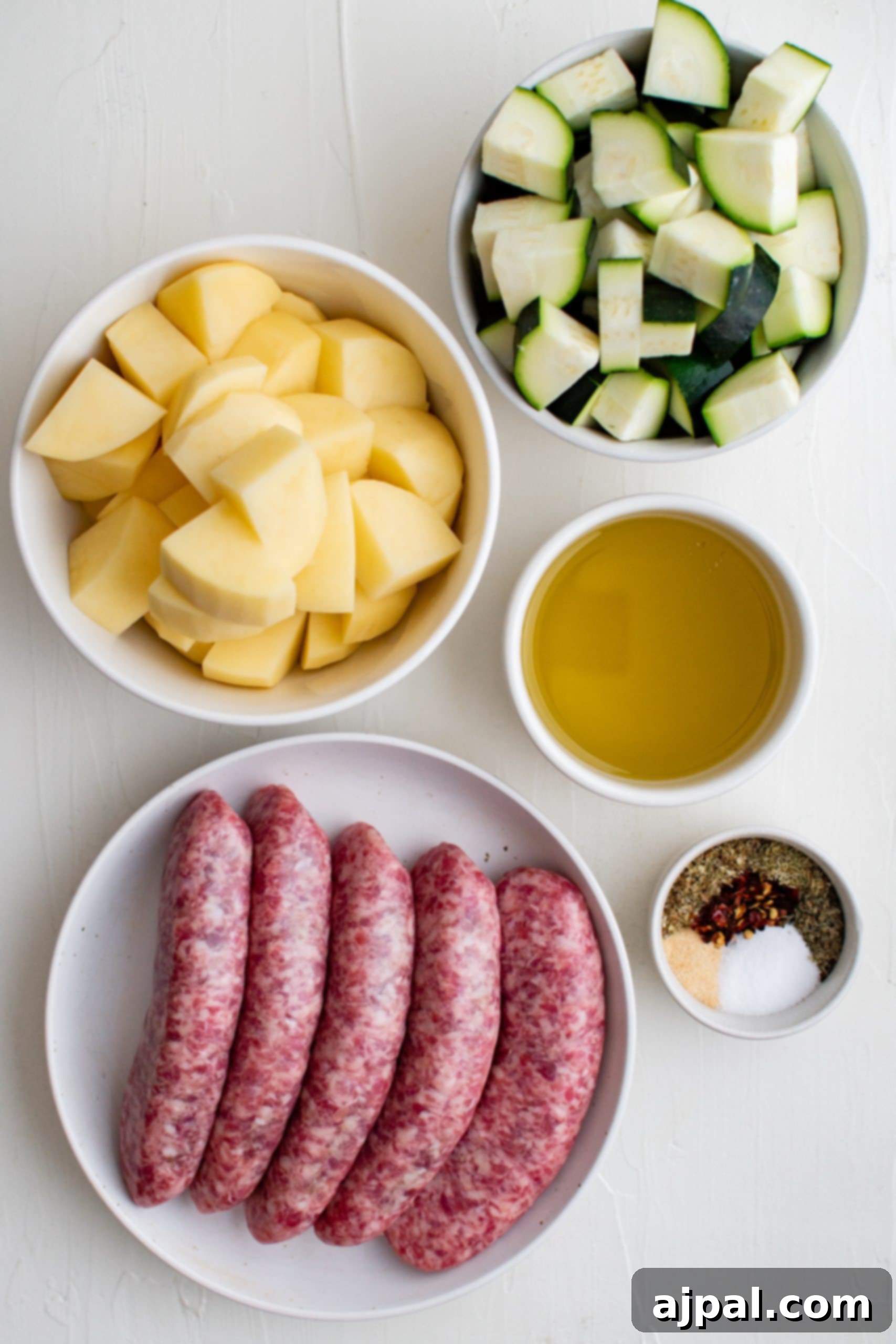 Simple Sheet Pan Sausage Dinner 11 Picture of sausage, potatoes, zucchinis, oil, and spices laid out on a table, ready for preparation.