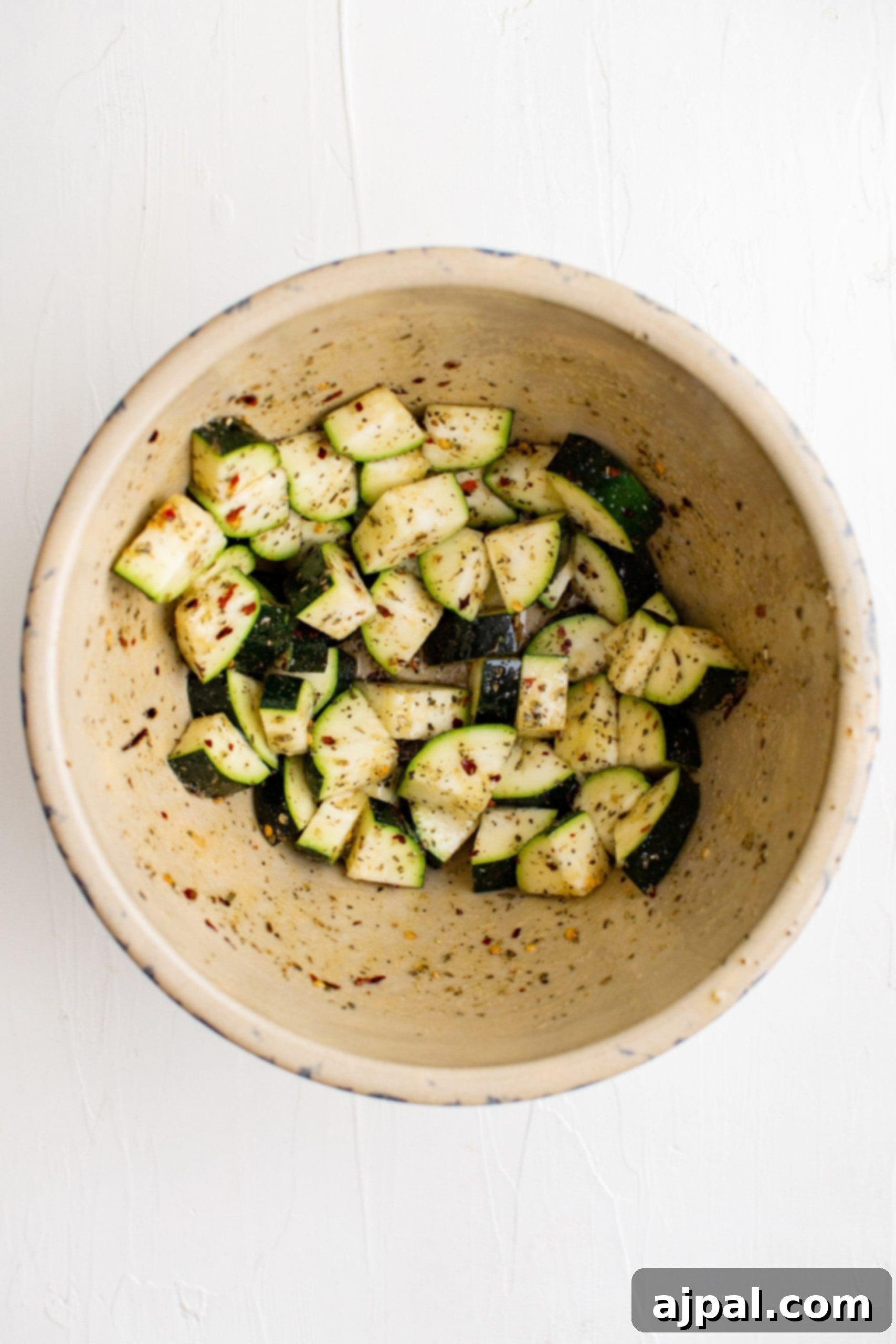 Simple Sheet Pan Sausage Dinner 14 Picture of zucchini diced and tossed in oil and spices in a bowl, prepared for roasting.